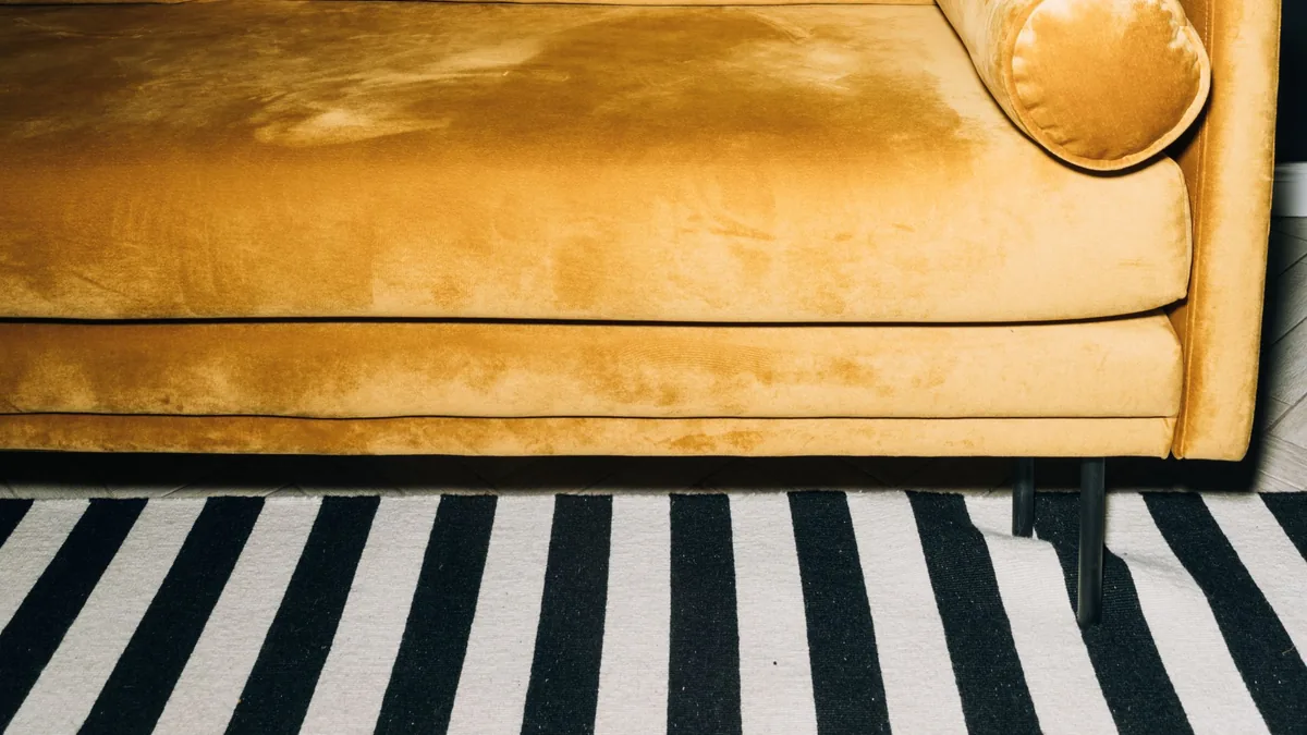 Detalhe de sofá amarelo manteiga com tecido aveludado e tapete listrado em preto e branco.