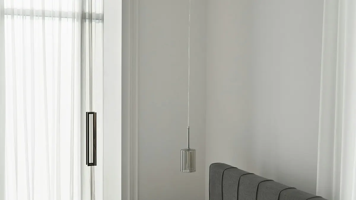 Quarto claro com cabeceira cinza baixa, janela ampla, parede suave e luminária pendente discreta.