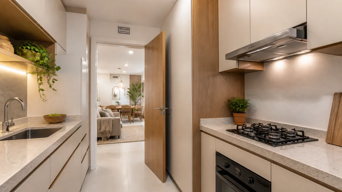 Cozinha pequena com coifa, grelha de ventilação livre e porta aberta para a sala.