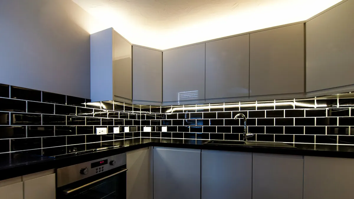 Cozinha cinza com azulejo preto brilhante, armários superiores claros e iluminação linear acima da bancada.