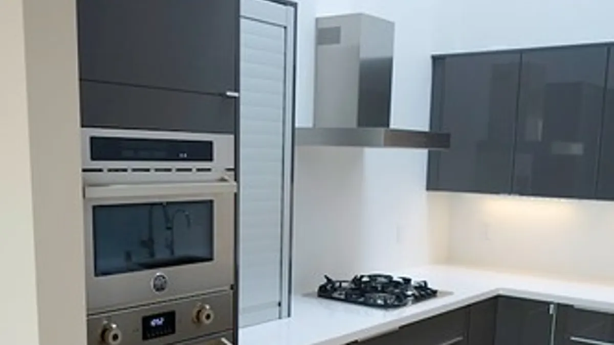 Cozinha compacta preta e cinza com bancada branca, armários escuros e luz sob os armários superiores.