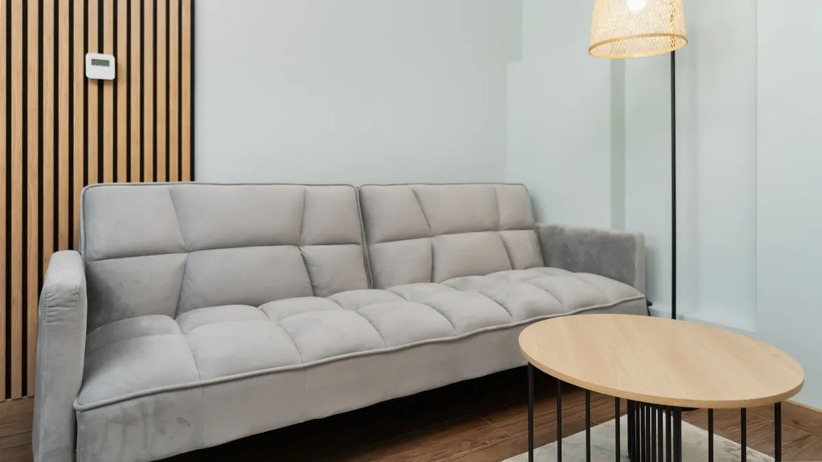 Sala de apartamento alugado com sofá cinza, quadros apoiados, luminária de piso, manta quente e mesa de madeira.